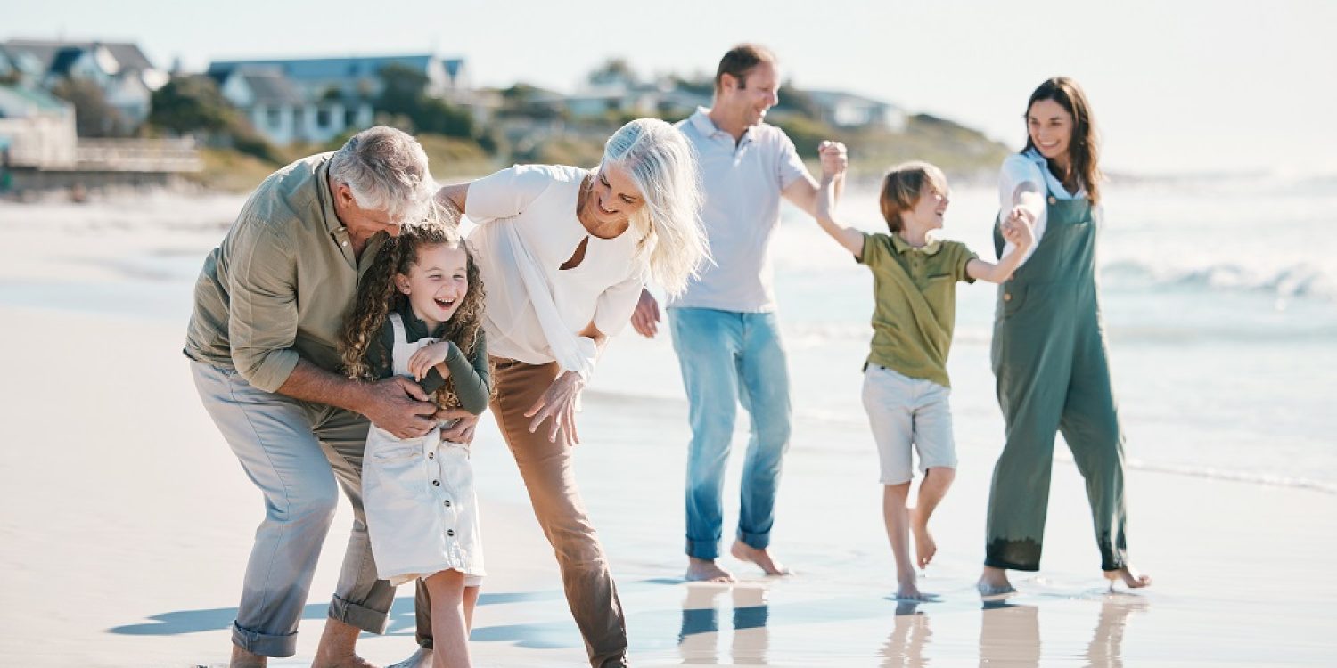 Grandparents, children and big family with play at beach, comic laugh or bonding for love, sunshine or excited on vacation. Mom, dad and kids by sea, waves and freedom on holiday for summer in Spain.